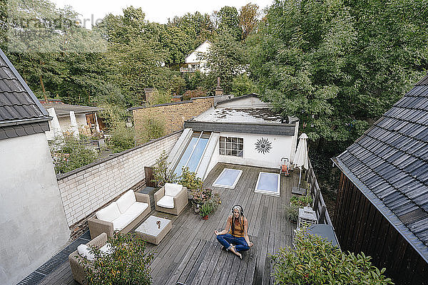 Frau mit Kopfhörern sitzt auf der Terrasse und macht Yoga-Übungen