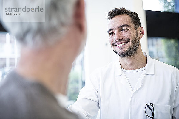 Mann im Arztkittel lächelt grauhaarigen Mann an