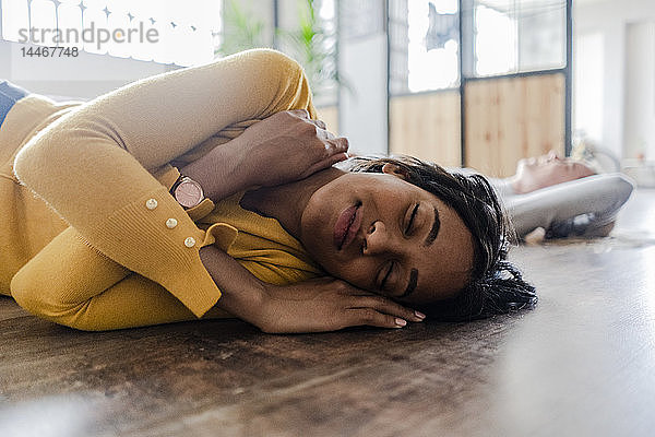 Lächelnde junge Frau mit geschlossenen Augen auf Holzboden liegend