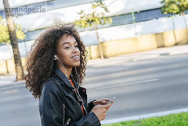 Porträt einer lächelnden jungen Frau  die mit Kopfhörern und Smartphone Musik hört