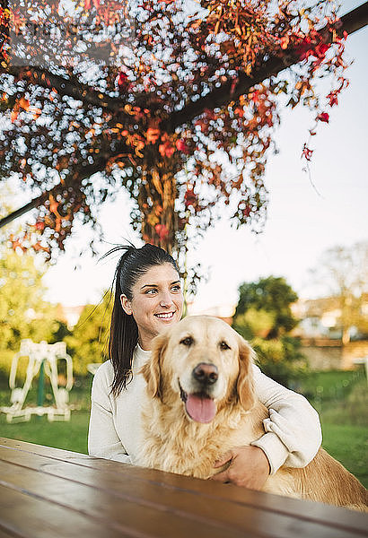 Lächelnde junge Frau mit ihrem Golden-Retriever-Hund  der sich in einem Park ausruht