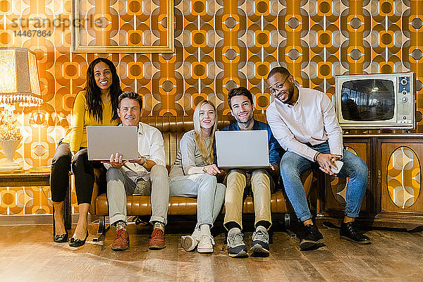 Gruppe von lächelnden Menschen  die auf einer Couch im alten Wohnzimmer mit Laptops sitzen