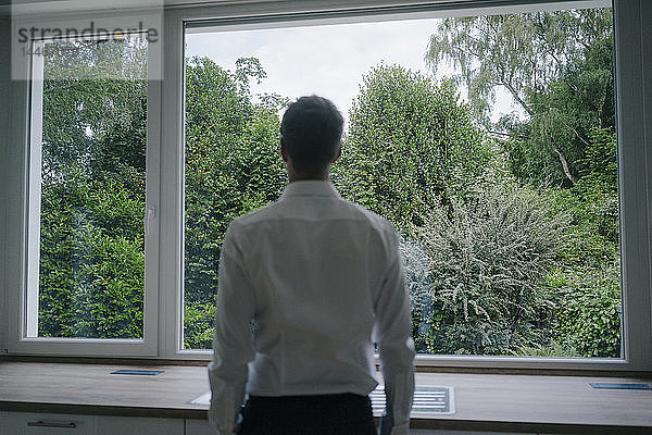 Geschäftsmann schaut aus dem Küchenfenster seines neuen Hauses  Rückansicht