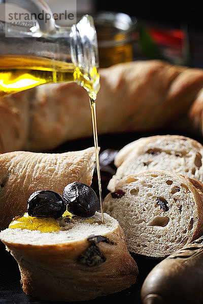 Gießen Sie Olivenöl auf eine Scheibe Ringbrot mit schwarzen Oliven