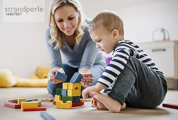 Lächelnde Mutter und Kleinkind spielen zu Hause mit Bausteinen