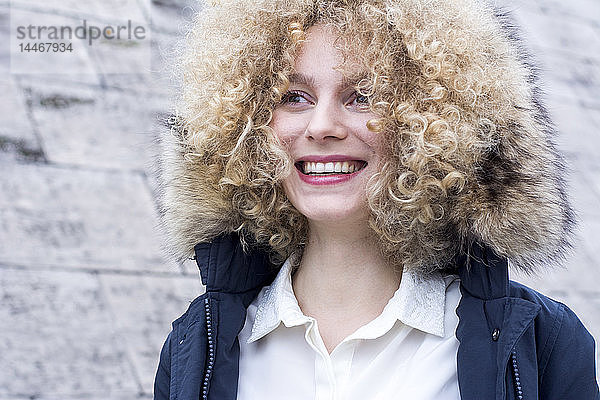 Porträt einer lachenden blonden Frau mit Ringellöckchen und Pelzkapuze