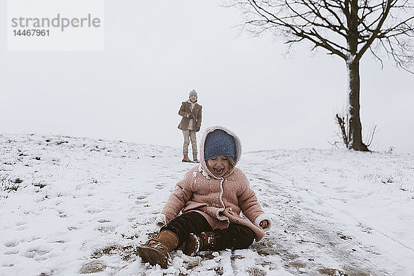 Weinendes Mädchen auf schneebedeckter Wiese mit Bruder im Hintergrund