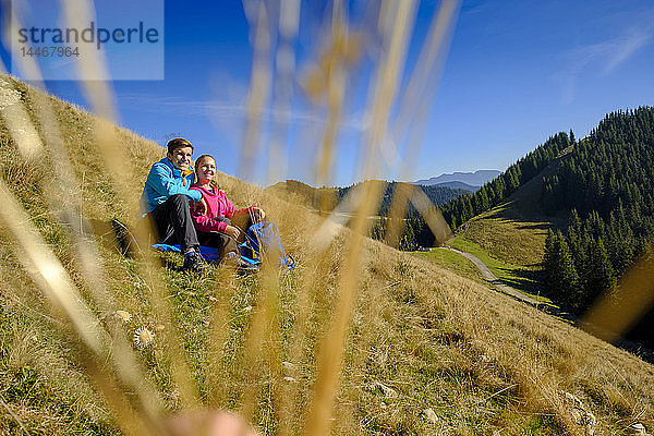 Deutschland  Bayern  Hoernle bei Bad Kohlgrub  glueckliches junges Paar bei einer Pause auf einer Wiese in alpiner Landschaft sitzend