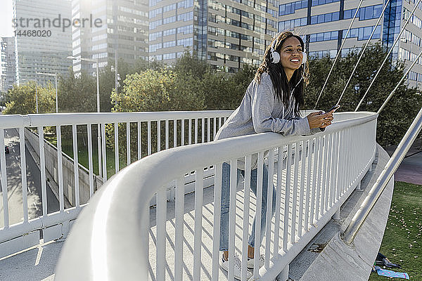 Junge Frau steht auf einer Brücke  hört Musik  benutzt ein Smartphone