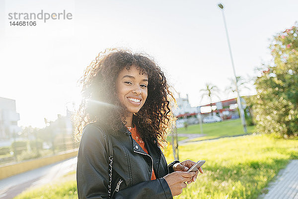 Porträt einer lächelnden jungen Frau mit Smartphone im Freien