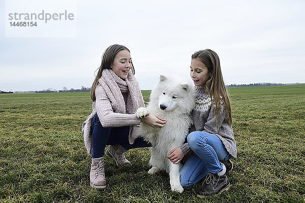 Zwei Mädchen kauern auf einer Wiese und unterrichtenden Hund