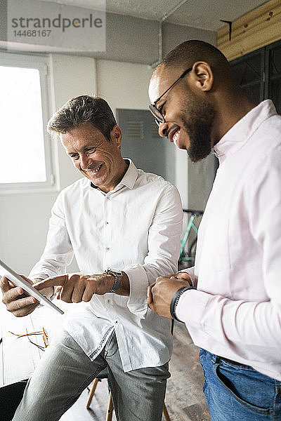 Zwei lächelnde Geschäftsleute mit Tabletten bei einer Besprechung im Loft-Büro