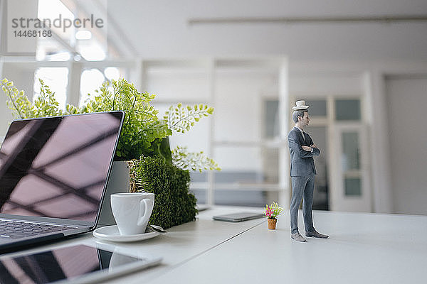 Geschäftsmann-Figur auf Schreibtisch stehend  eine Tasse Kaffee auf dem Kopf balancierend