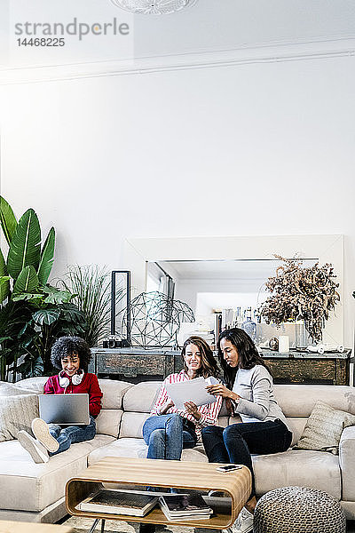 Drei Frauen mit Laptop und Dokumenten auf der Couch sitzend