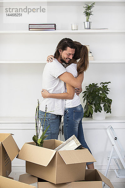 Paar mit Pappkartons umarmt sich im neuen Zuhause