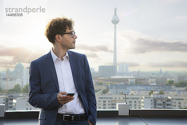 Deutschland  Berlin  Geschäftsmann mit Smartphone auf der Dachterrasse am Abend