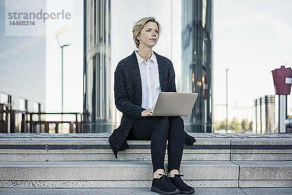 Junge Geschäftsfrau sitzt auf einer Treppe und benutzt einen Laptop