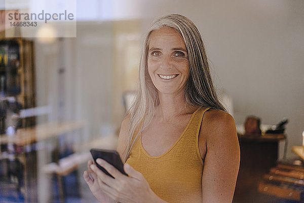 Porträt einer lächelnden Geschäftsfrau mit Handy in ihrem Geschäft
