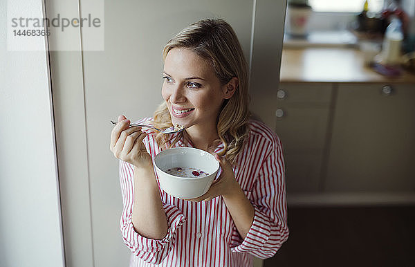 Lächelnde Frau frühstückt morgens zu Hause