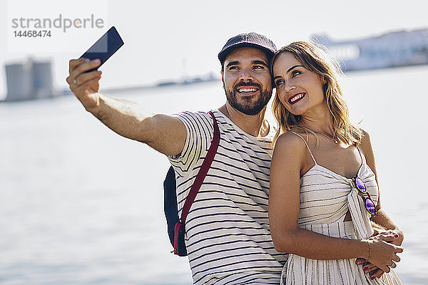 Spanien  Andalusien  Malaga  glückliches Touristenpaar  das sich an der Küste mit einem Smartphone selbstständig macht
