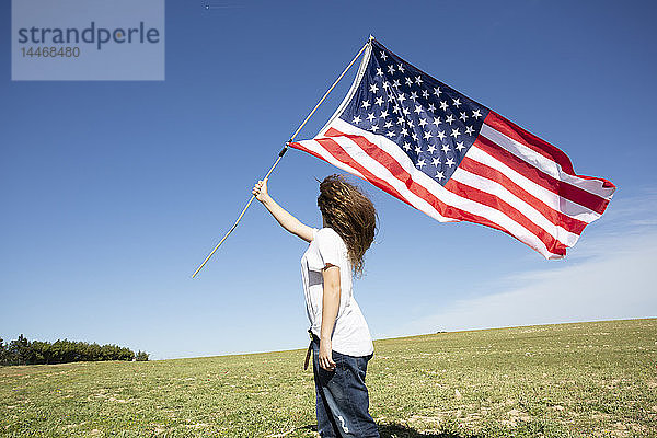 Mädchen mit amerikanischer Flagge auf Feld in entlegener Landschaft