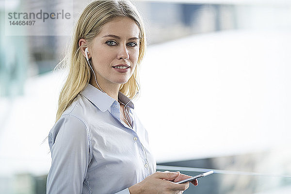 Porträt einer blonden Frau mit Smartphone und Kopfhörern