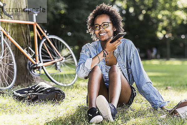 Lächelnde junge Frau ruht sich mit Handy und Tablet im Park aus