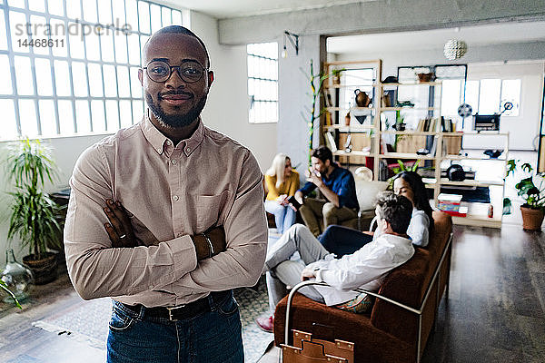 Porträt eines lächelnden jungen Geschäftsmannes mit Mitarbeitern im Hintergrund in einem Loft-Büro