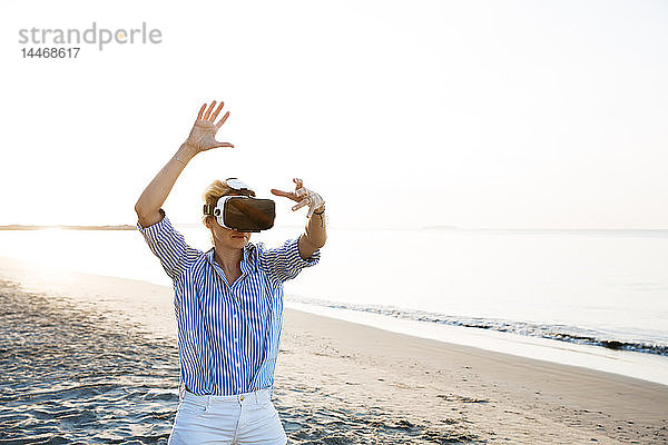 Blonde Frau macht eine Art Yoga-Übungen an einem Strand in Thailand mit einer 3D-Brille für virtuelle Realität