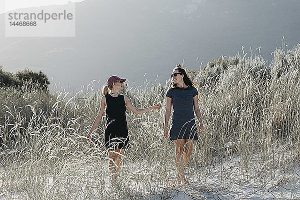 Südafrika  Western Cape  Hout Bay  zwei junge Frauen  die in den Dünen spazieren gehen und dabei sprechen