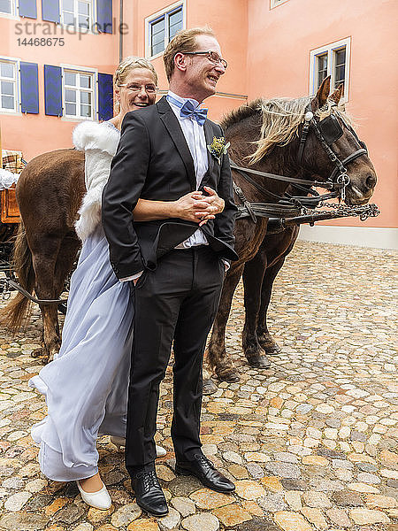 Glückliche Braut und Bräutigam auf Kopfsteinpflasterplatz mit Kutsche