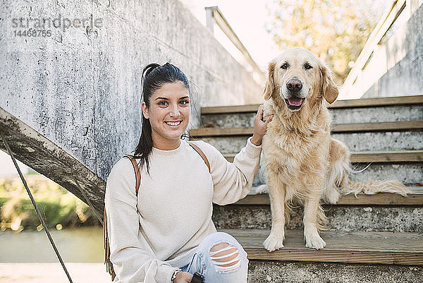 Porträt einer lächelnden jungen Frau mit ihrem Golden-Retriever-Hund auf einer Treppe im Freien