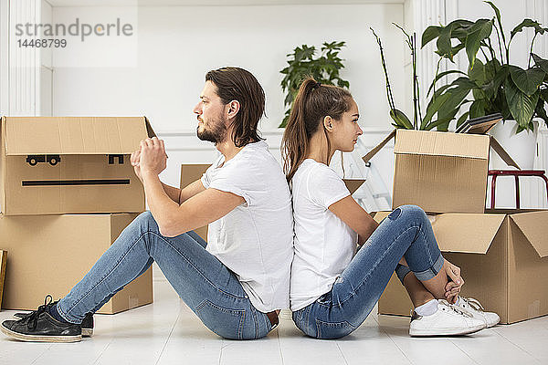 Paar mit Pappkartons auf dem Boden sitzend in neuer Wohnung