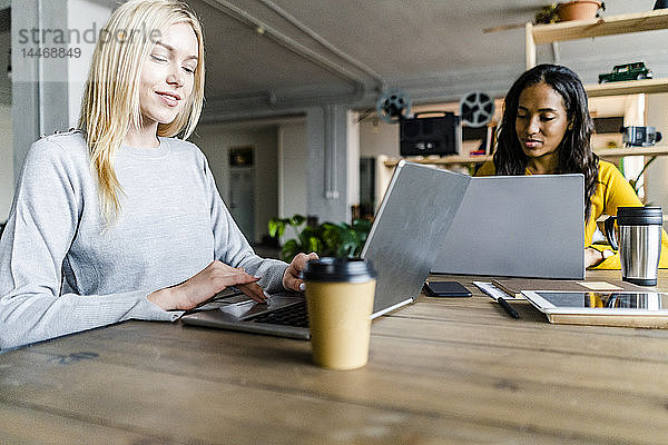 Zwei junge Geschäftsfrauen sitzen am Konferenztisch im Loft-Büro und benutzen Laptops
