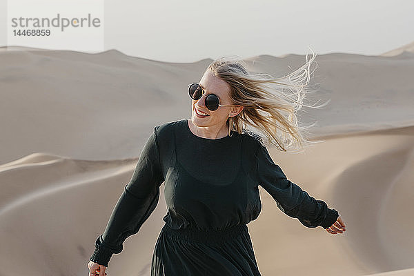 Namibia  Namib  Porträt einer lächelnden Frau mit wehendem Haar  die auf einer Wüstendüne steht