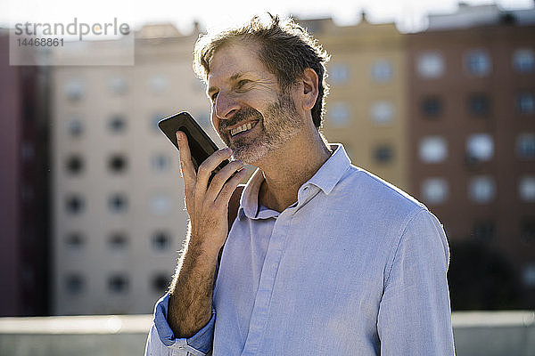 Lächelnder reifer Mann benutzt Mobiltelefon in der Stadt