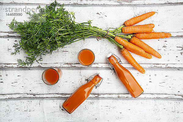Karotten  Gläser mit Karottensaft und Bügelverschlussflaschen auf Holz  von oben
