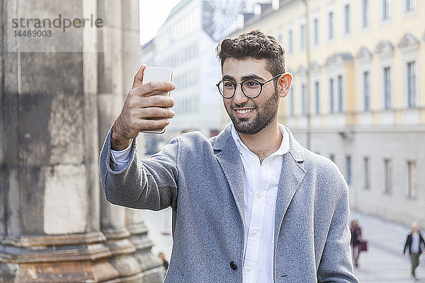 Deutschland  München  Porträt eines jungen Geschäftsmannes  der in der Stadt mit dem Handy Selbsthilfe betreibt