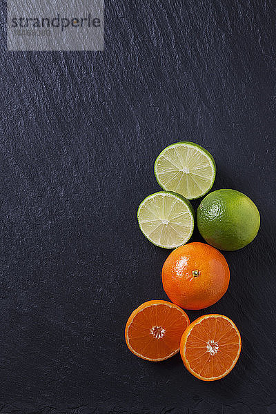 Limetten und Mandarinen auf schwarzer Schiefertafel