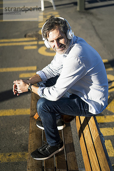 Reifer Mann sitzt auf einer Bank und hört Musik mit Kopfhörern