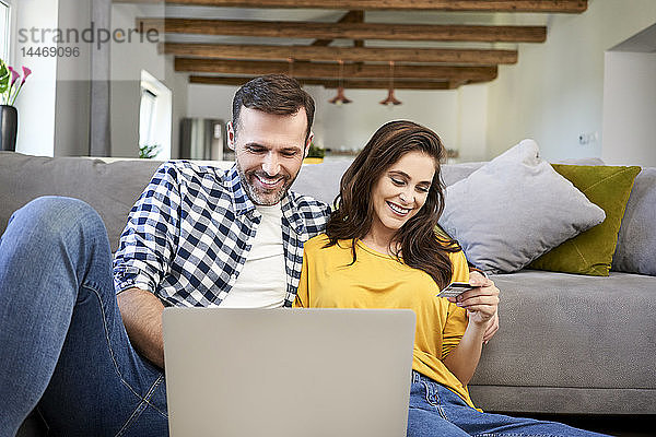 Ehepaar  das im Wohnzimmer sitzt  einen Laptop benutzt und eine Online-Zahlung mit seiner Kreditkarte tätigt