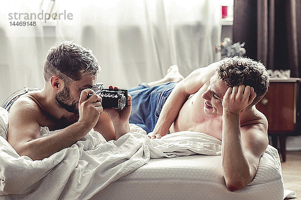 Schwuler Mann fotografiert seinen Partner mit altmodischer Kamera im Bett
