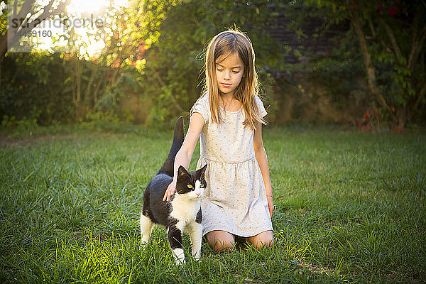 Porträt eines kleinen Mädchens  das eine Katze im Garten streichelt