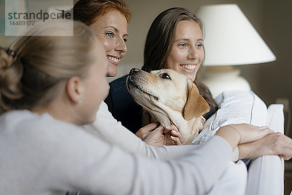 Glückliche Mutter mit zwei Mädchen im Teenager-Alter und Hund auf der Couch zu Hause
