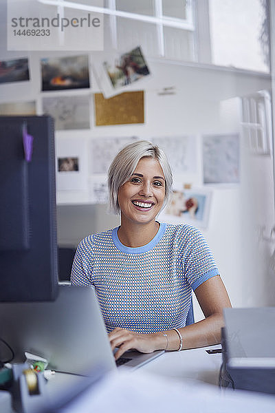 Junge Frau  die im Büro arbeitet  am Schreibtisch sitzt und lächelt