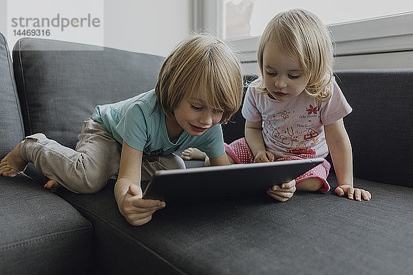 Bruder und kleine Schwester benutzen digitales Tablet auf der Couch zu Hause