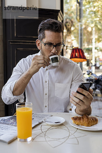 Geschäftsmann frühstückt in einem Cafe und überprüft sein Handy