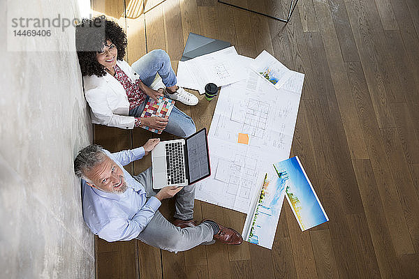 Geschäftsmann und Geschäftsfrau sitzen auf dem Boden in einem Loft und arbeiten mit Laptop und Dokumenten