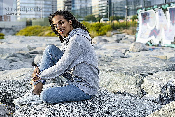 Junge Frau sitzt auf Felsen am Strand und entspannt