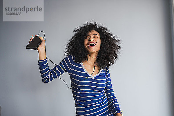 Porträt einer glücklichen jungen Frau mit Smartphone und Kopfhörern beim Singen und Tanzen